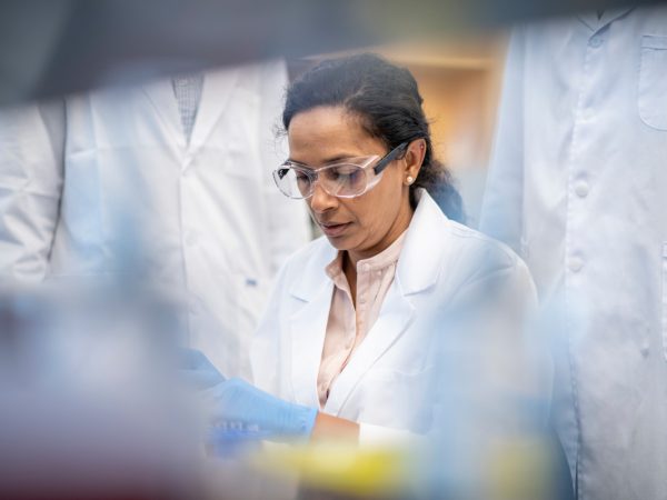 Female chemistry professor using a pipette in the lab with students observing her actions A mature, mixed race, female biochemist conducting an experiment in a laboratory using a pipette with students making observations.