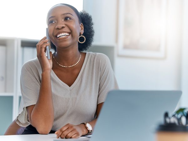 Happy business woman smile talking on phone call or young entrepreneur answering cellphone while sitting in front of work laptop in an office. Female executive smiling and laughing at a funny joke.